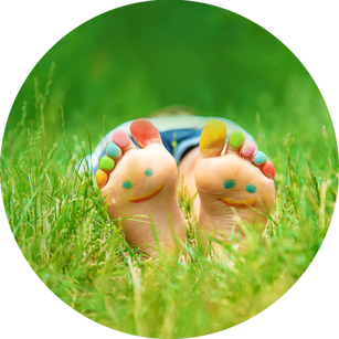 Child laying in the green grass with paint on toes